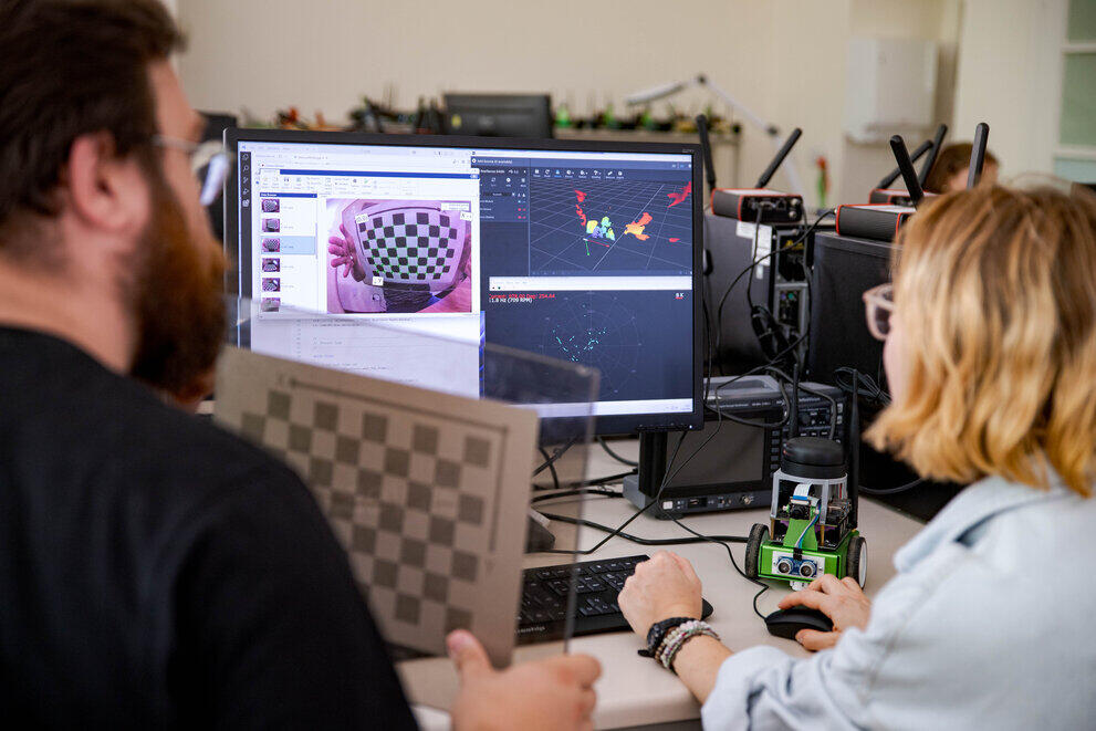 Two people are testing a small robot on a computer in the laboratory