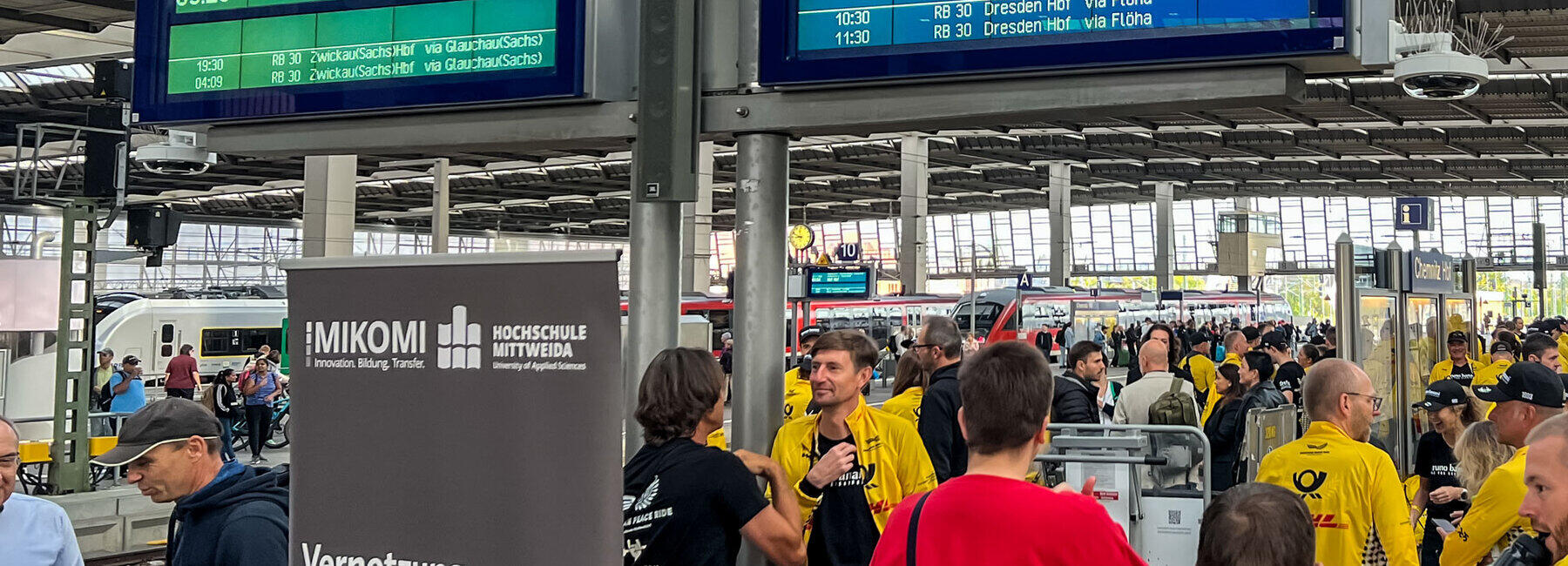 Menschen, darunter viele Sportler im gelben DHL-Trikot an einem Bahnsteig.