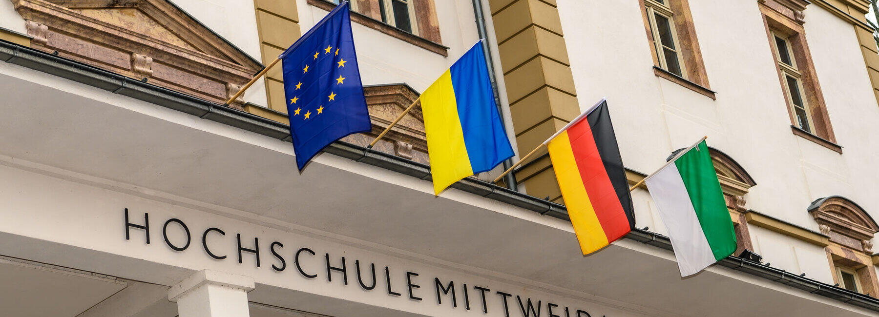 Vier Flaggen über dem Eingansgportal des Hauoptgbäudes der Hochschule Mittweida: Europa, Ukraine, Deutschland und Sachsen.
