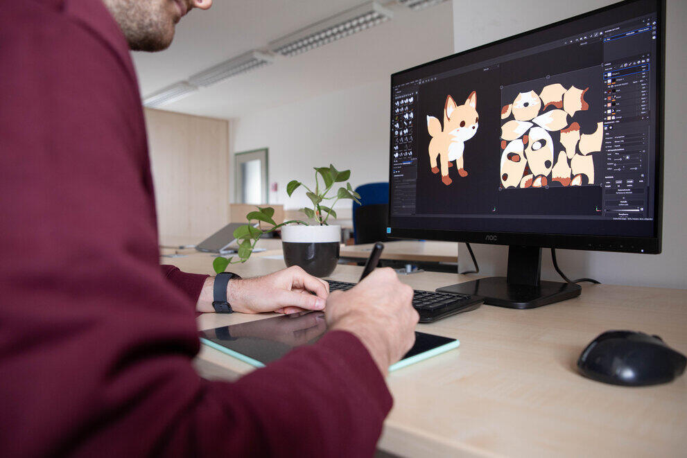 Ein Student sitzt vor einem PC-Bildschirm und zeichnet auf seinem Tablet.