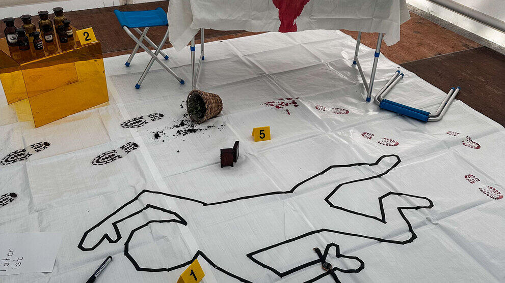 Eine Szenerie mit einem Umriss von einer Person auf dem Boden. Ringsum sind verschiedene Spuren erkennbar: Fußabdrücke, Blut, umgeworfene Gegenstände..