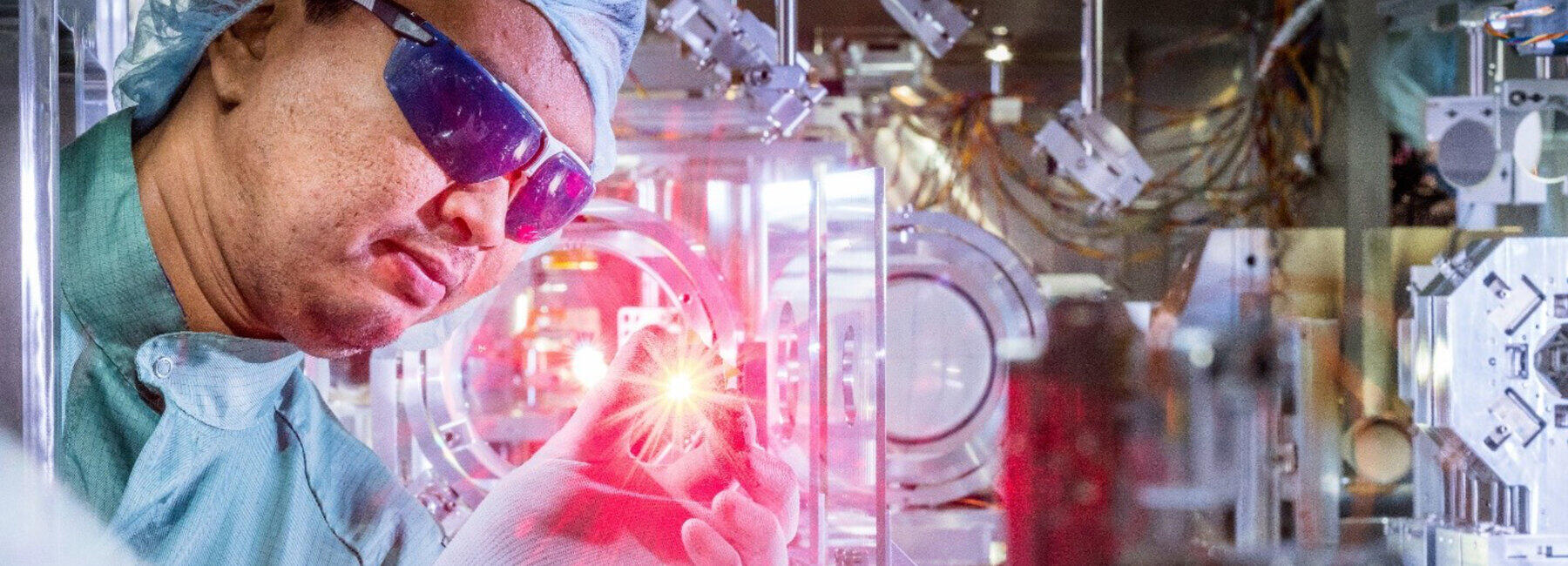 Person in Reinraumschutzkleidung untersucht eine leuchtende Probe umgegeben von technischen Geräten