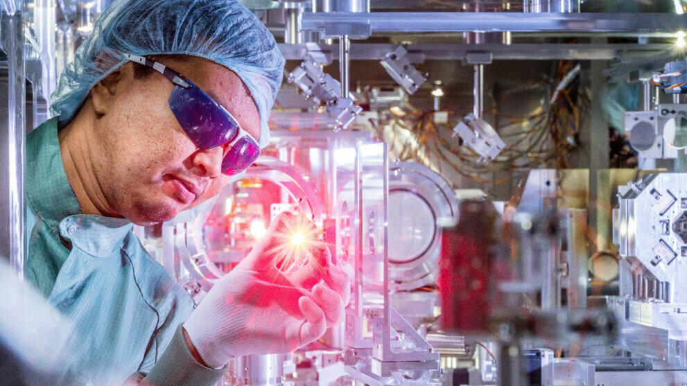 Person in Reinraumschutzkleidung untersucht eine leuchtende Probe umgegeben von technischen Geräten