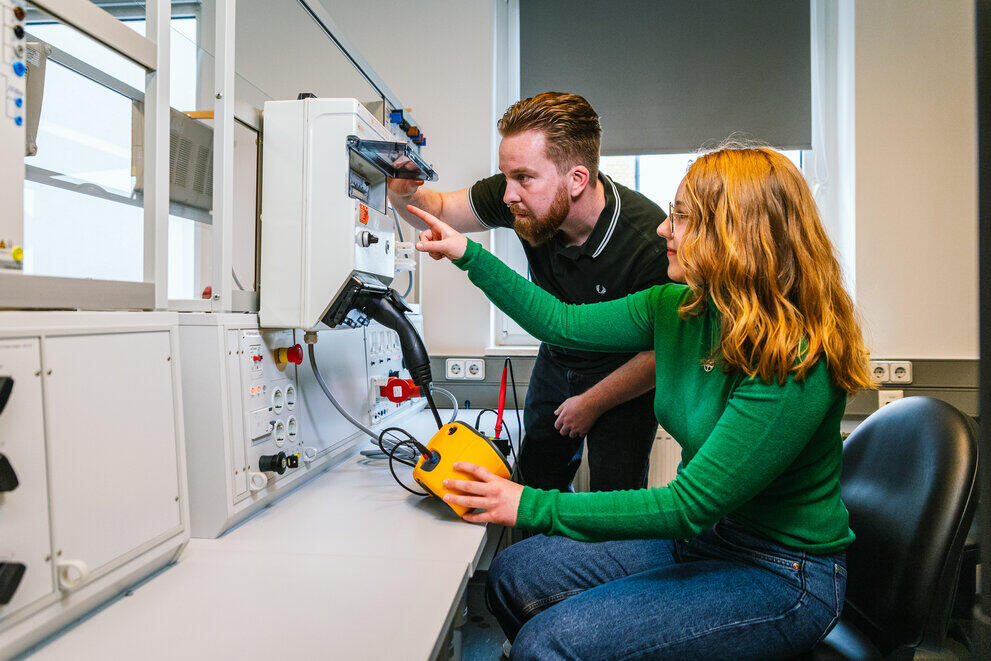 Zwei Studierende sitzen vor einem elektronischen Versuchsstand und nehmen Messwerte.