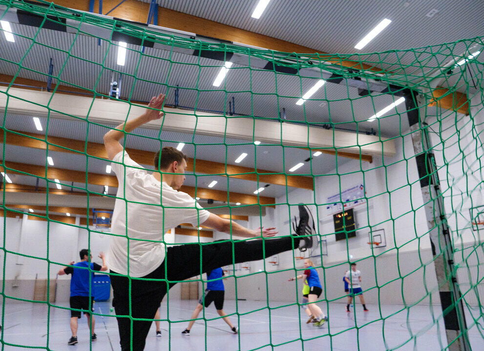 Ein Handball-Torwart versucht artistisch mit hochgerissenem rechten Bein einen Ball abzuwehren.