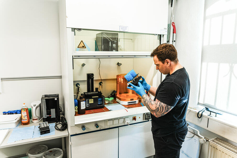 Ein Mann steht in einem Labor und hält ein 3D-gedrucktes Element in der Hand