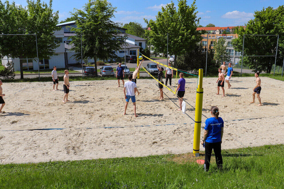 Zwei Teams spielen gegeneinander Beachvolleyball. Der Ein Spieler am Netz versucht mit einer Streckung den Ball zu erreichen.