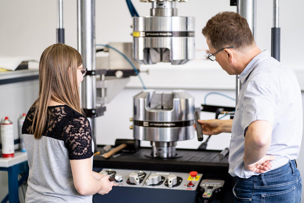 A lecturer is explaining something to a student using a hydraulic wedge clamping unit.