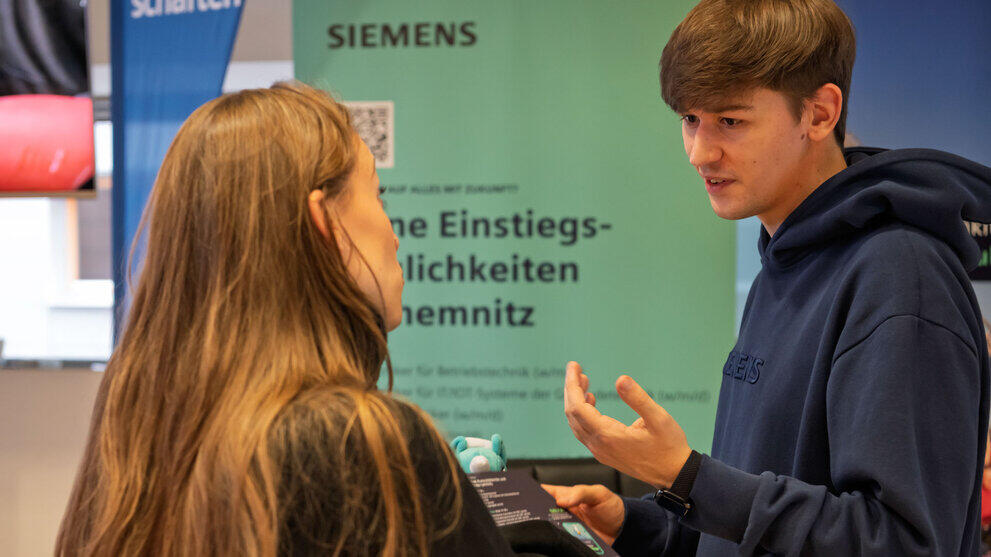 A young woman and a young man talking in front of a ‘Siemens’ roll-up banner