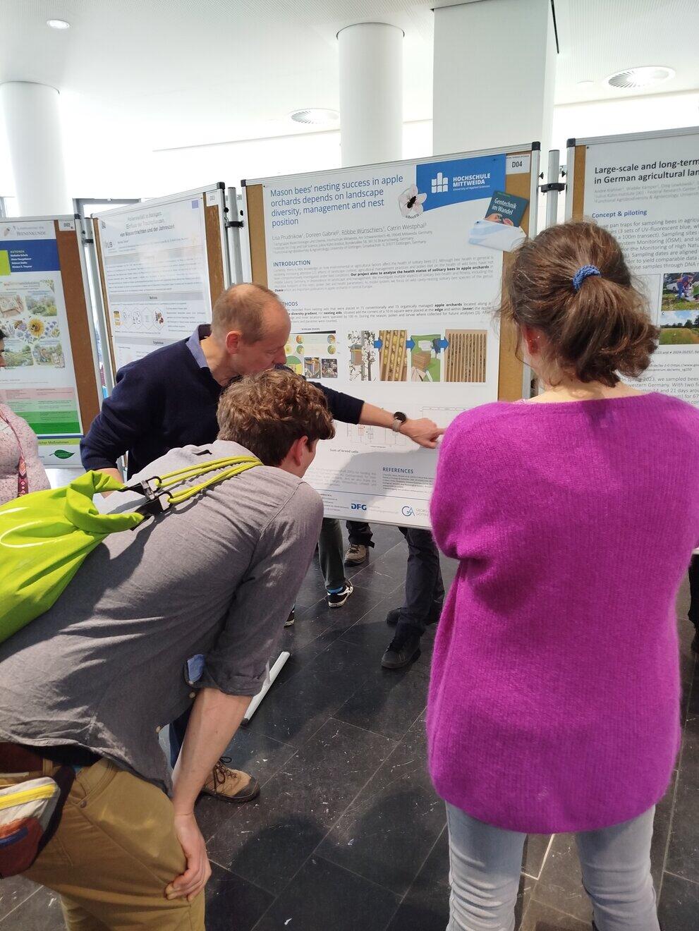 One person explains something using a poster; two people are listening