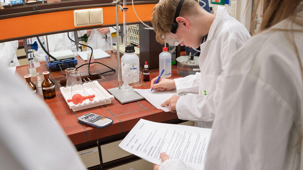 Schüler:innen in Laborkitteln an einem Labortisch