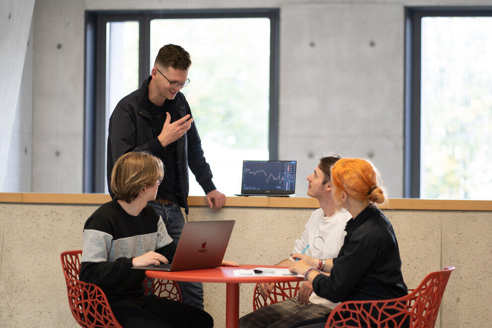 Vier Studierende sitzen an einem Tisch und unterhalten sich.