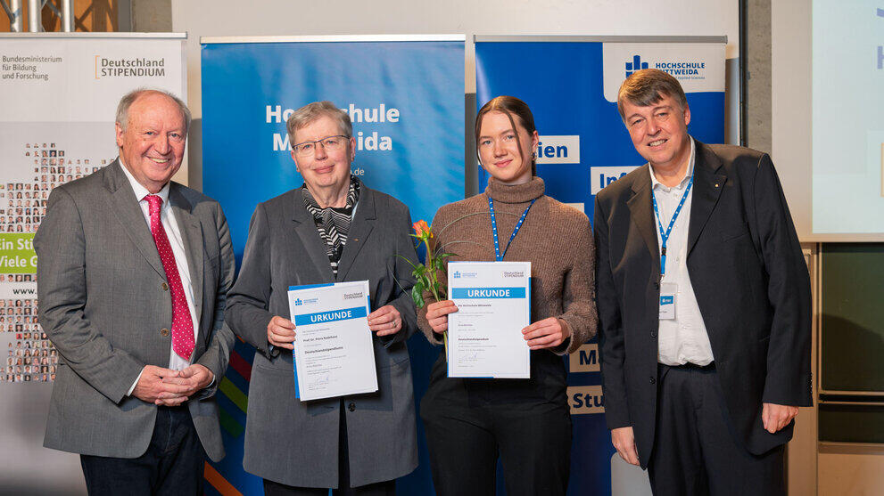 Zwei weibliche Personen mit Urkunden zwischen den Übergebenden.