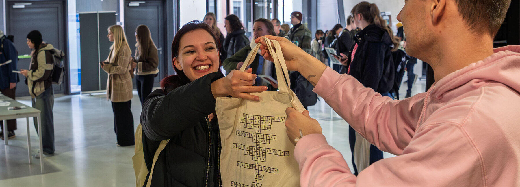 A woman with a beaming smile is handed a cloth bag across a counter by a man.