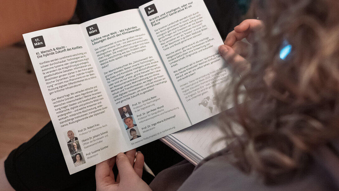 Blick über die Schulter einer weiblichen Person, die den aufgeschlagenen Dialog Kontrovers Flyer in den Händen hält. Zu sehen sind die Beschreibngen der ersten beiden und des letzten Abends.
