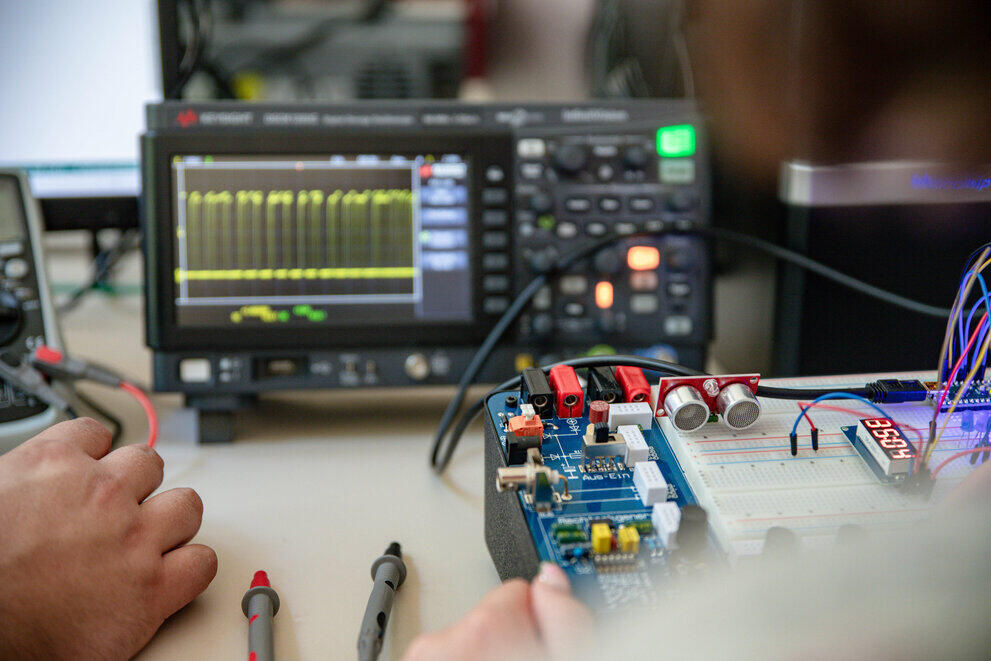 A person is testing an electronic circuit using an oscilloscope and test probes in the laboratory