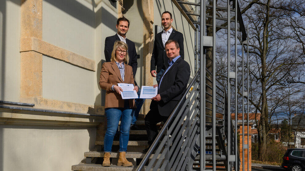 Vier Personen auf einer Treppe mit dem Jahresarbeitspapier in den Händen