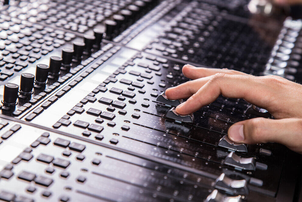 A hand is adjusting the controls on a mixing desk.