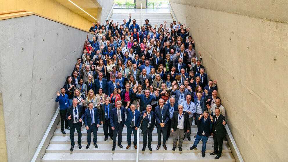 All the conference participants are standing on the steps of the Ludwig Hilmer Building at the university, waving cheerfully at the camera.