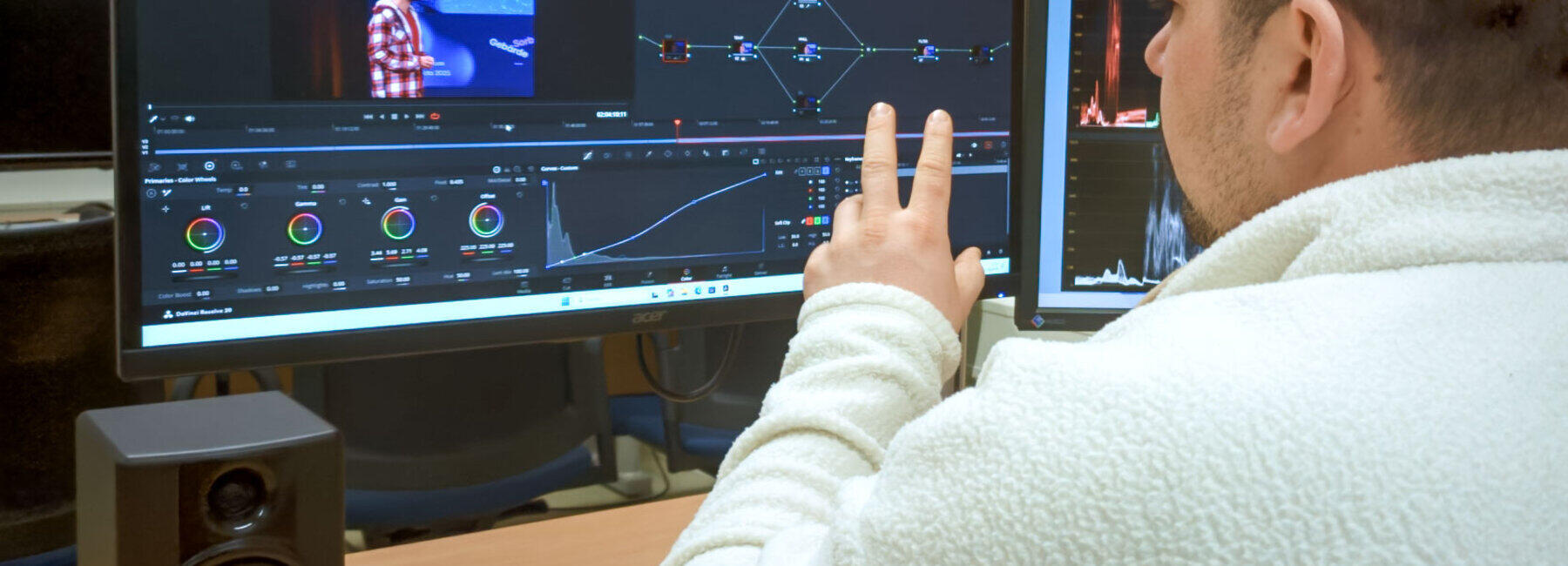 A close-up shot of a person sitting at a desk from behind, in front of a large monitor.