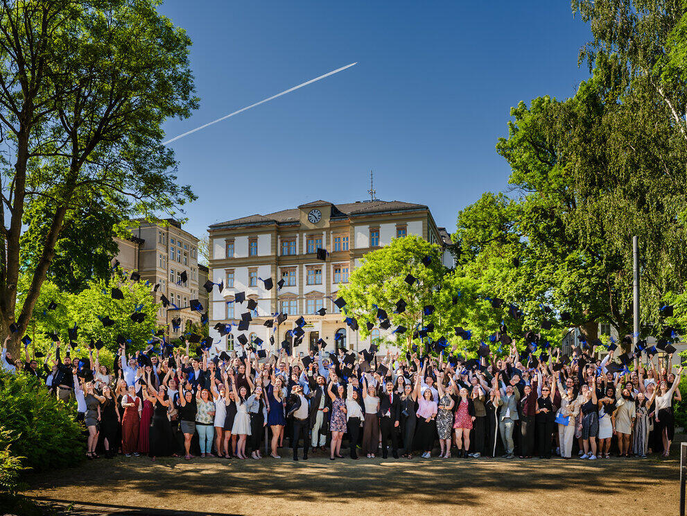 Gruppe junger Alumni beim traditionellen Hütewerfbild vor Haus 1