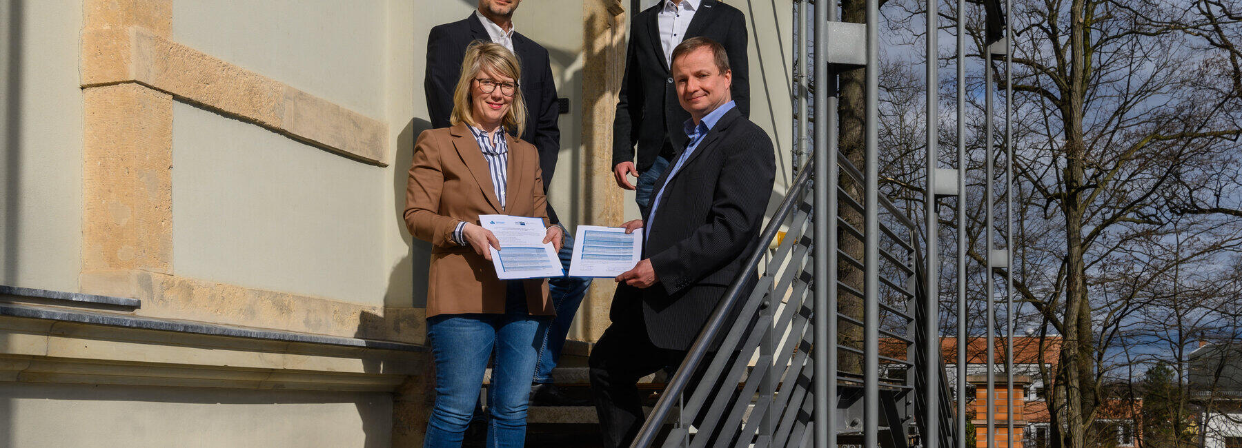 Vier Personen auf einer Treppe mit dem Jahresarbeitspapier in den Händen