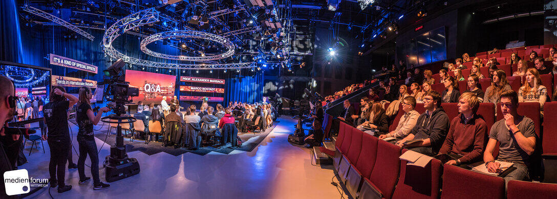 A panoramic view of a packed television studio with audience seating.