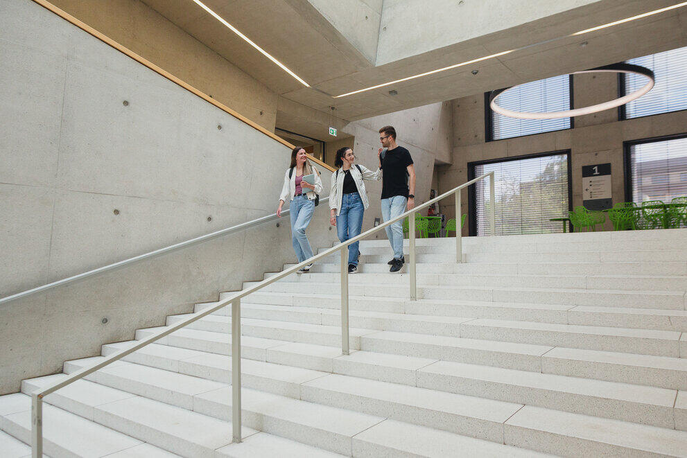 Three students are walking down a flight of stairs together in a modern building.