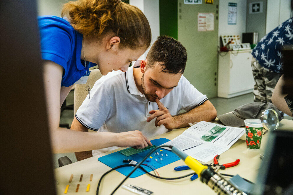 In the soldering lab, a member of staff is helping a visitor to assemble an electronic component.