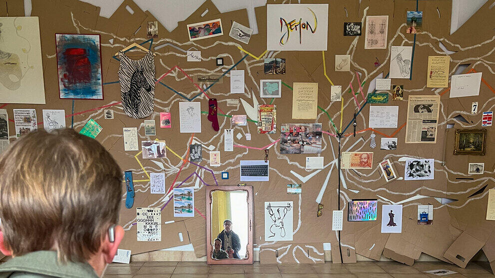 Eine Wand mit verschiedensten Elementen, meistens Gedrucktes wie an den verzweigten Ästen eines Baume hängend angeordnet.