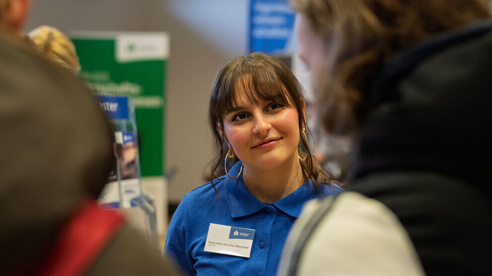 A young woman wearing a blue HSMW polo shirt, deep in conversation.