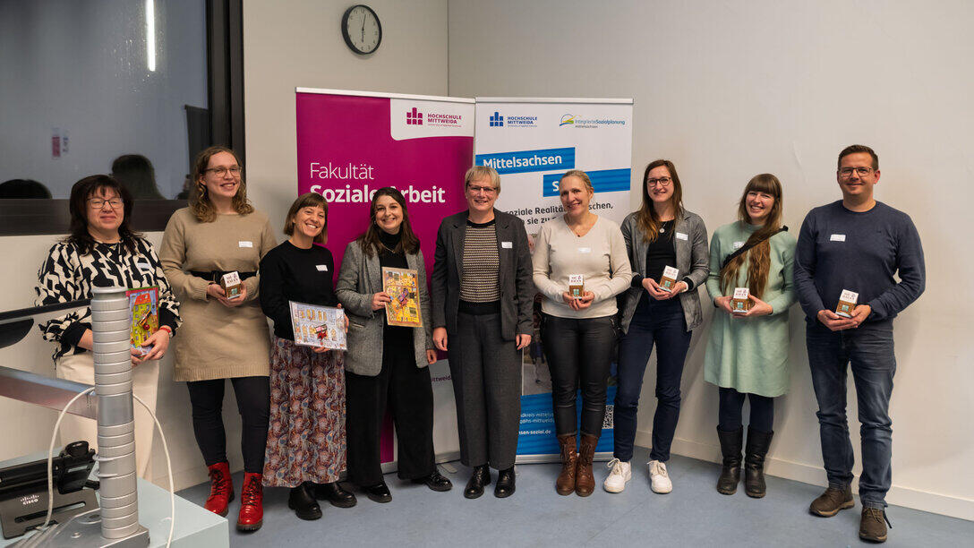 A group of eight women and one man at the front of the lecture theatre, in front of roll-up banners reading ‘Faculty of Social Sciences’ and ‘Mittelsachsen Sozial’