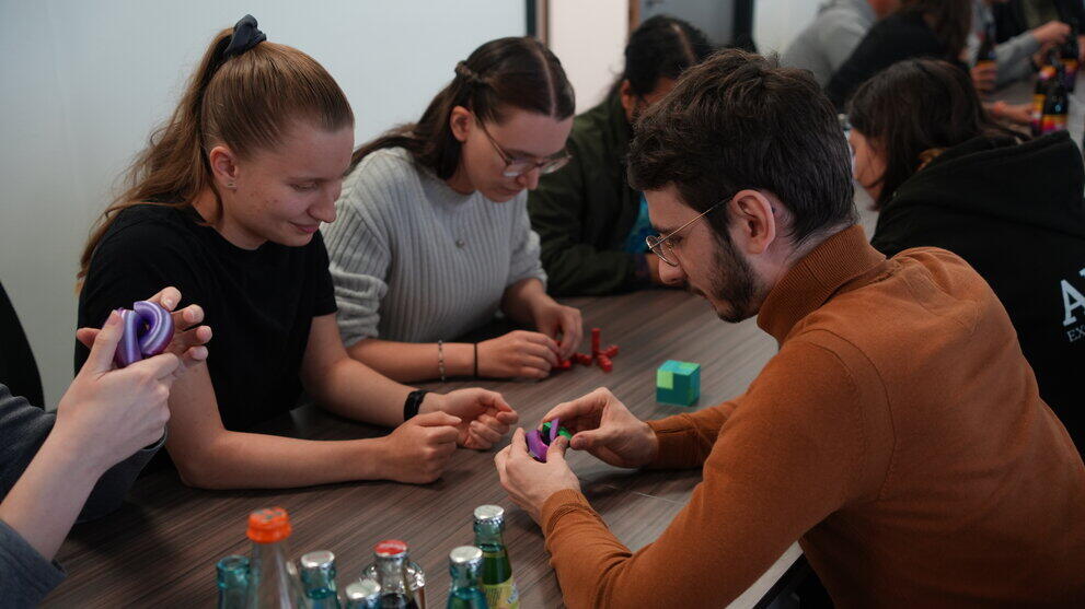 Personengruppe sitzt lächelnd am Tisch und puzzelt