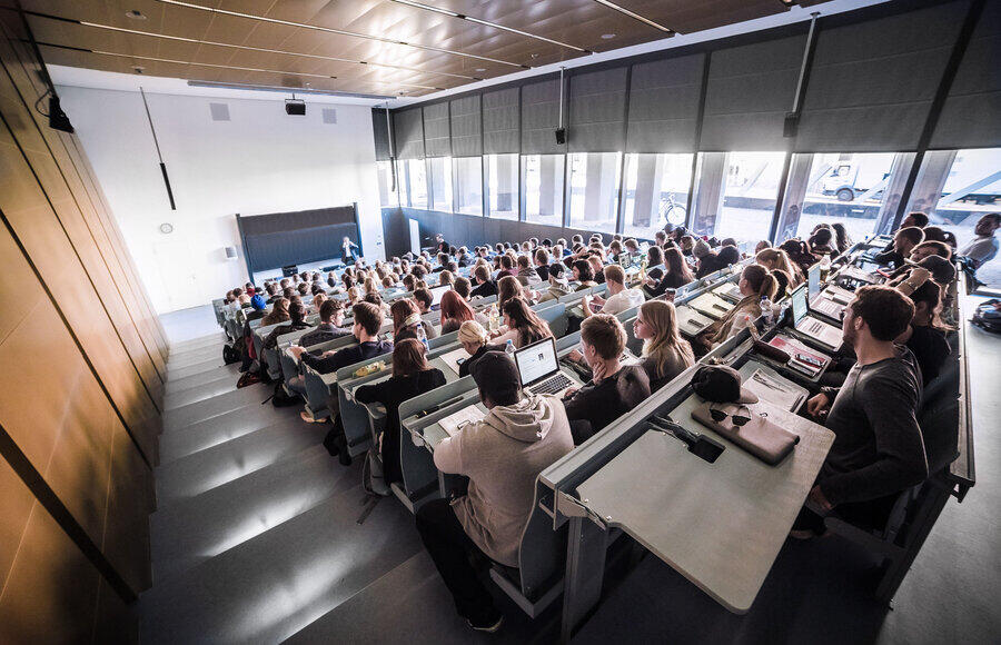 Hörsaal mit vielen Studierenden, die auf Reihenplätzen sitzen und einem Dozenten zuhören, der vor einer Tafel steht