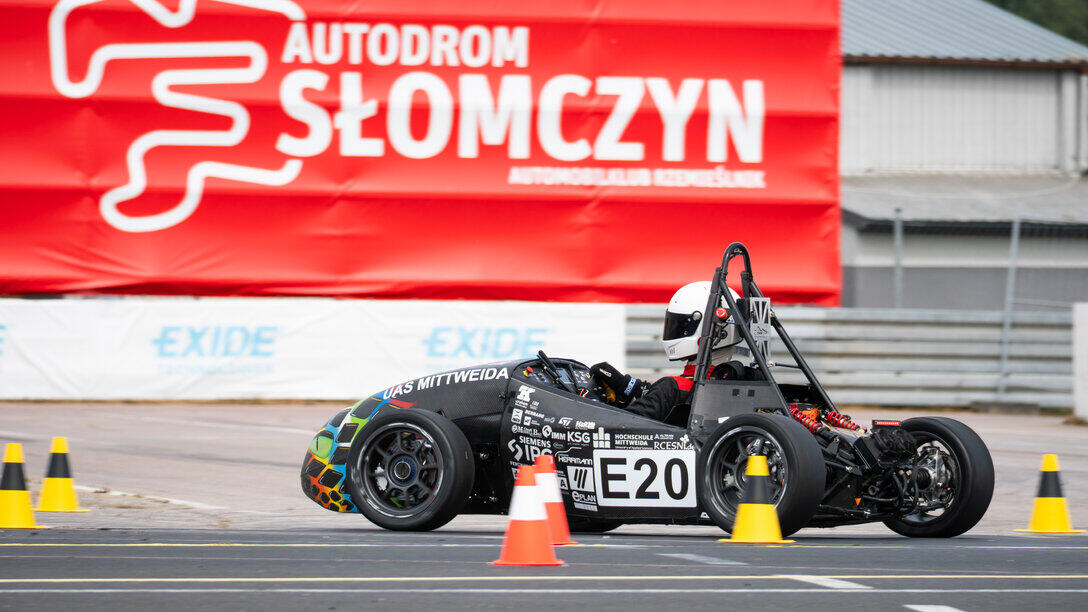 Formula Student Rennwagen von TMM auf der Rennstrecke zwishen Pylonen. Im Hintergrund ist auf einem großen Transparent Autodrom Słomczyn zulesen
