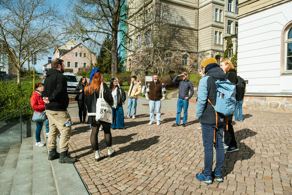 Eine Gruppe Studieninteressierter und deren Eltern stehen vor einem Hochschulgebäude. Studentische Guides erzählen vom Studienalltag.