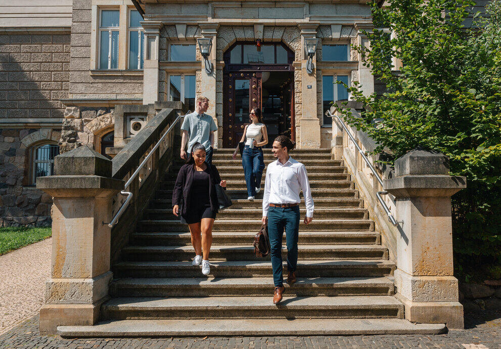Four students are walking down a flight of stairs in front of a building together.