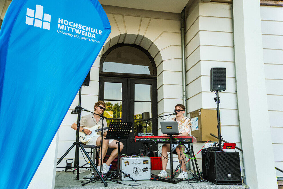 Two musicians are playing music on an electric guitar and a keyboard in the entrance hall of the main building.