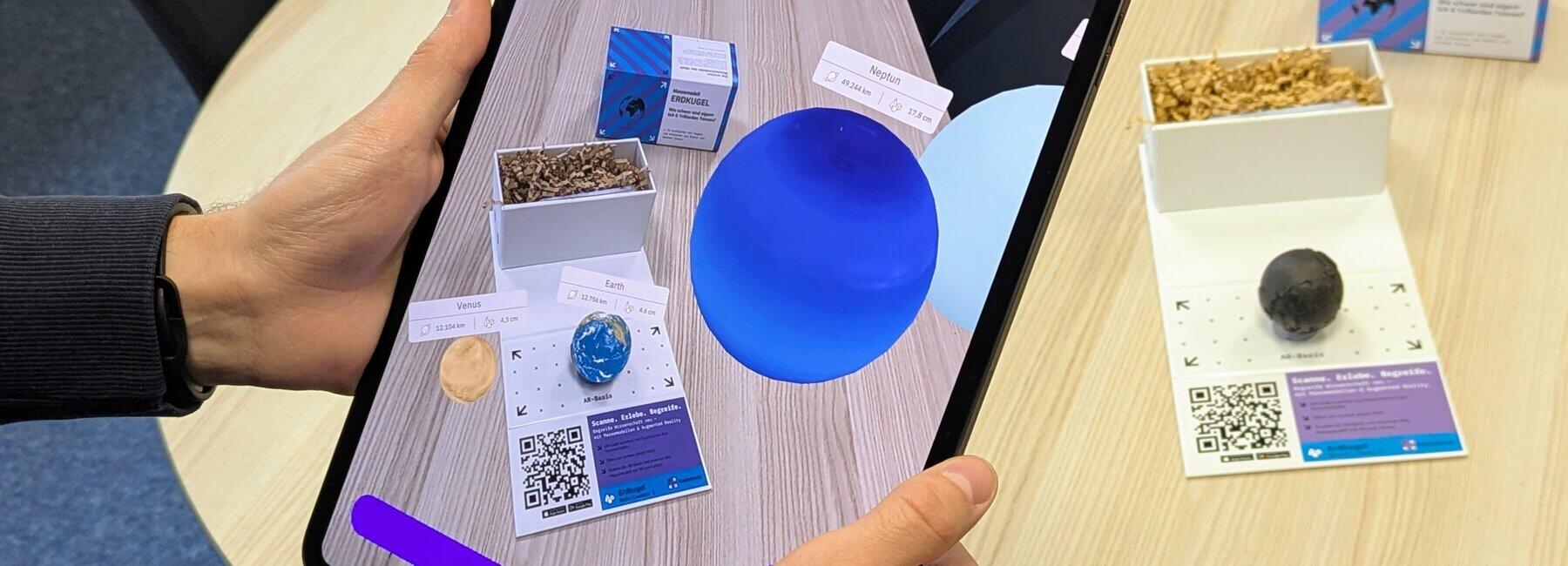 Two hands are holding a tablet in front of a table with models on it