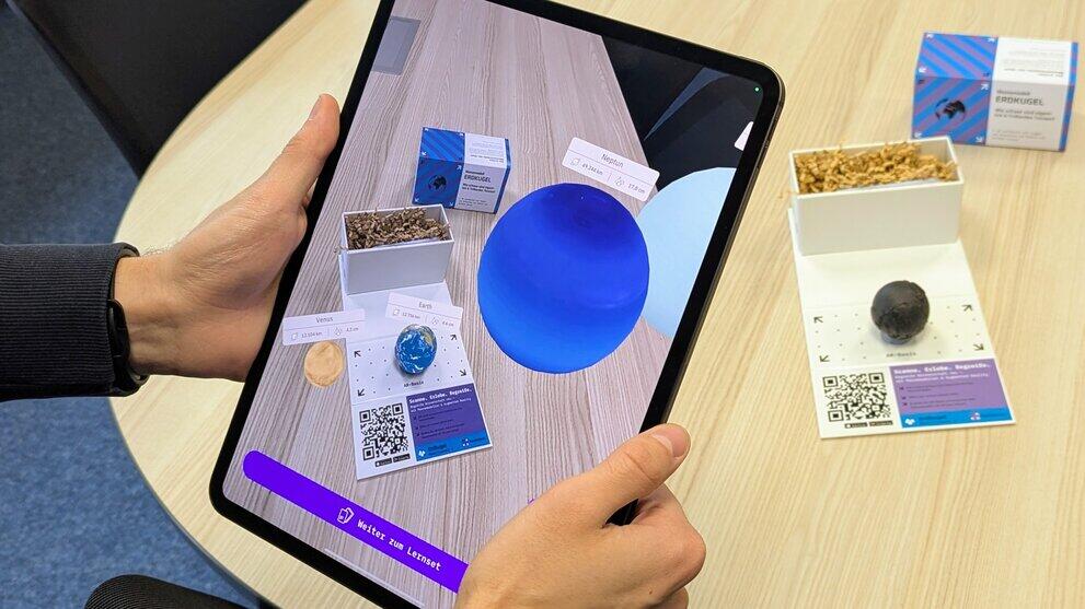 Zwei Hände halten ein Tablet vor einem Tisch mit Modellen