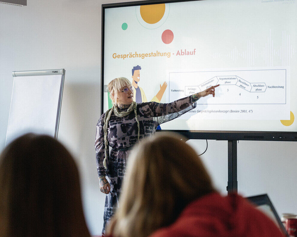 A student is standing in front of a digital whiteboard, pointing at a diagram.