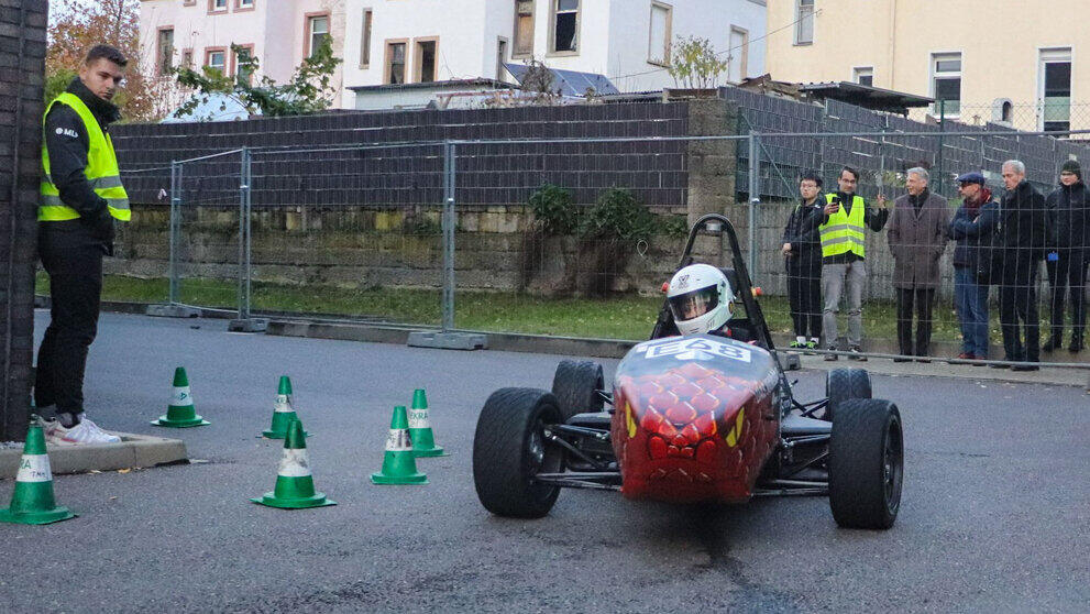 Rennauto fährt vor Zuschauenden im Hintegrund hinter Bauzäunen.
