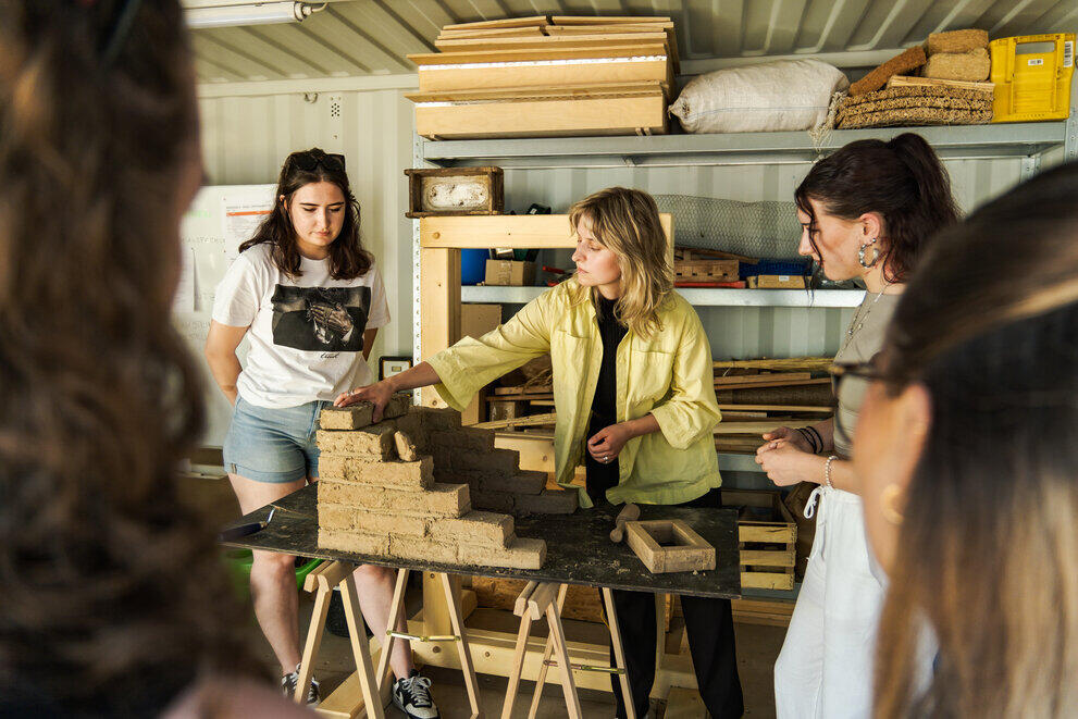 A lecturer explains a clay-based construction method to students during a practical session.