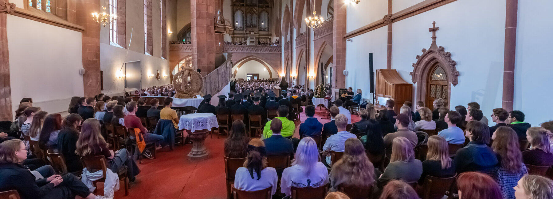 A view from the chancel into the packed nave. A large harvest wreath stands between the heads of young people and the heads of professors, adorned with doctoral caps.
