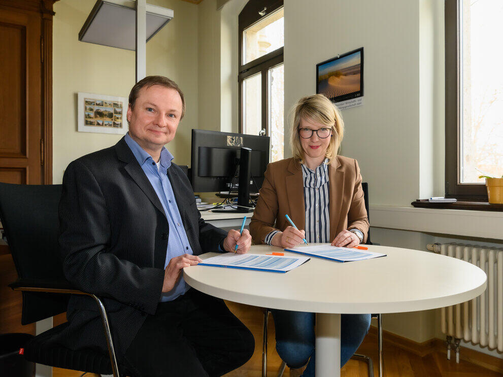 Zwei Personen sitzen am Tisch und unterschreiben ein Dokument