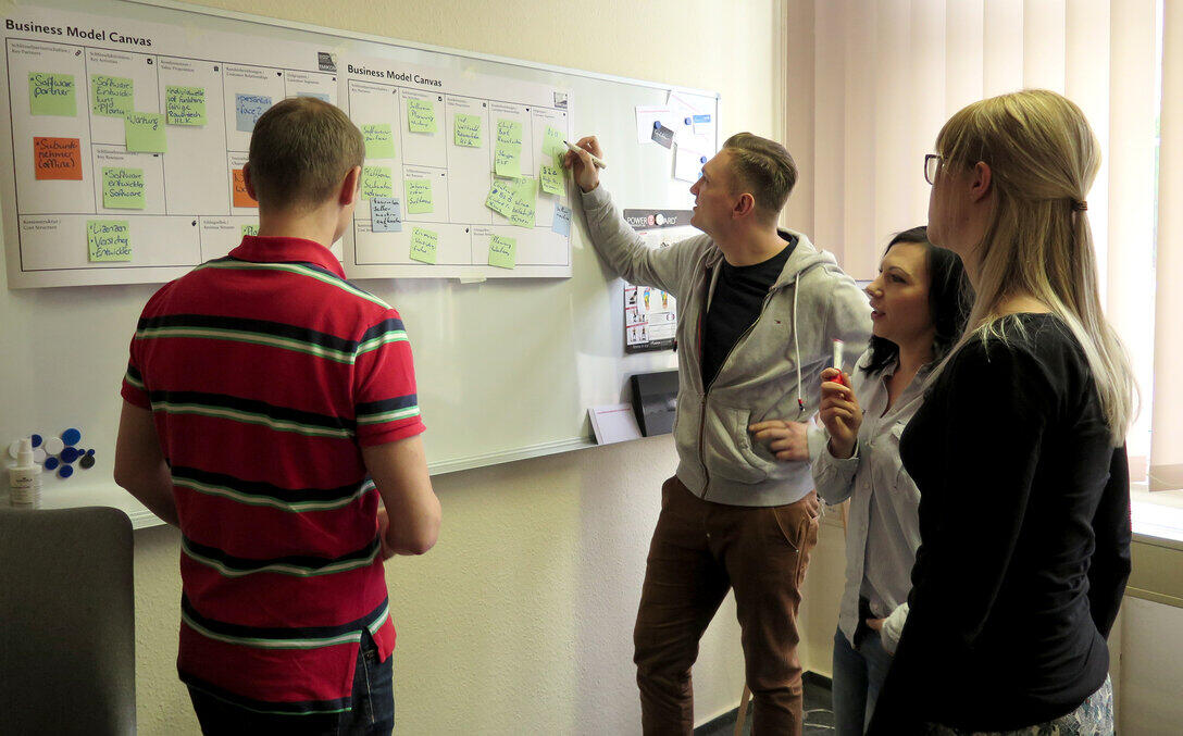 Zwei Frauen und zwei Männer stehen vor einem Whiteboard, an dem Zettel hängen.