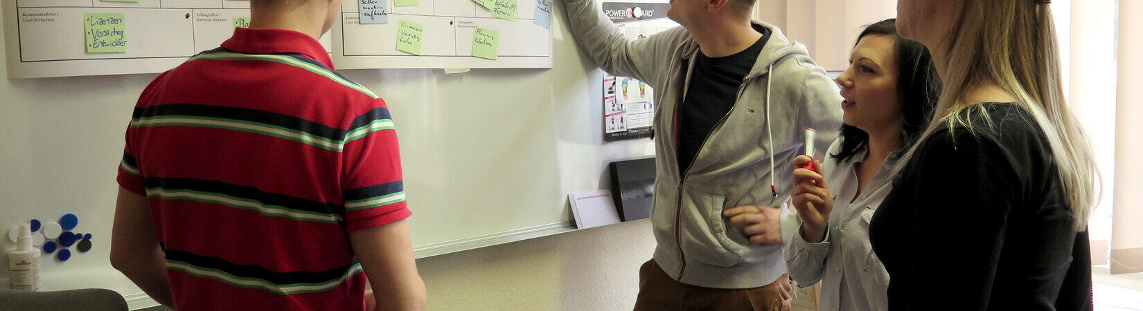 Zwei Frauen und zwei Männer stehen vor einem Whiteboard, an dem Zettel hängen.