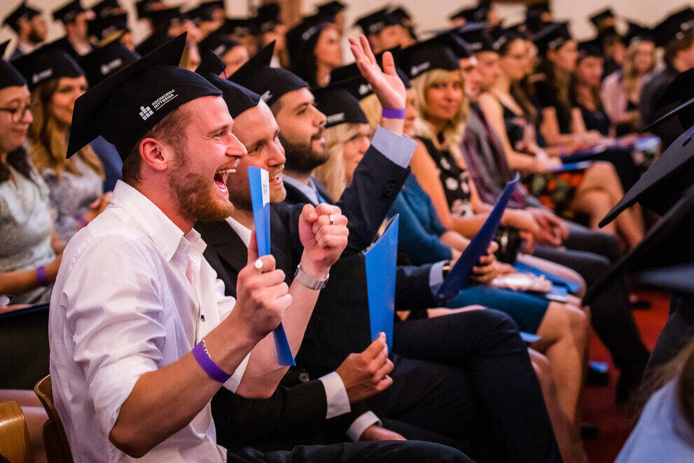 Alumni mit Hut und Urkunde machen Foto in Siegerpose