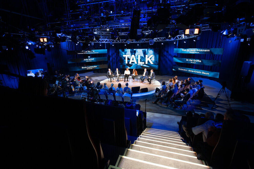 Auf der Bühne eines TV-Studios sitzen mehrere Personen während einer Podiumsdiskussion.