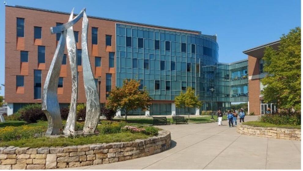 Campus grounds: a square with a sculpture, people, and buildings in the background